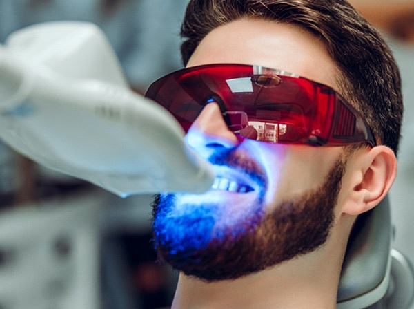 A young male with a beard wearing protective eyewear while receiving in-practice teeth whitening