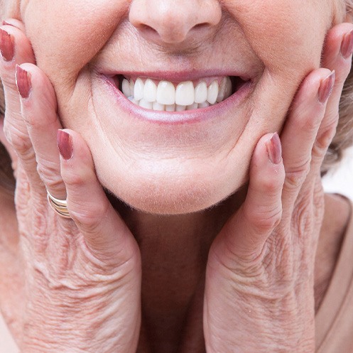 Nose-to-neck view of woman with dentures smiling while touching her cheeks