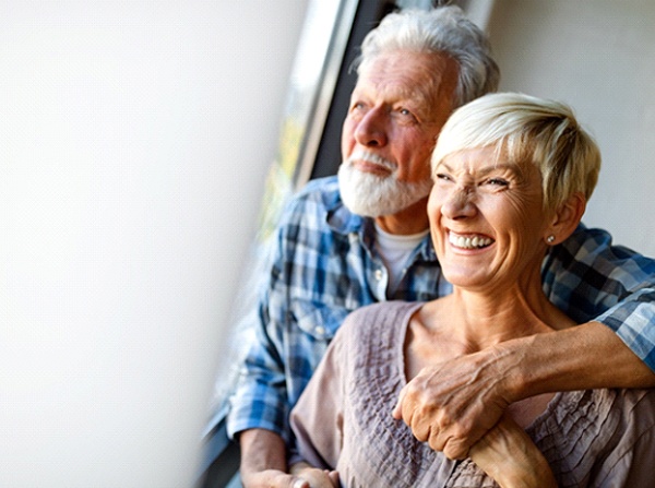 An older couple hugging and smiling while showing off their new and improved dental implants