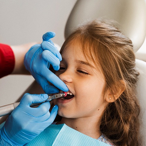 Hygienist in blue gloves polishing a girl’s teeth