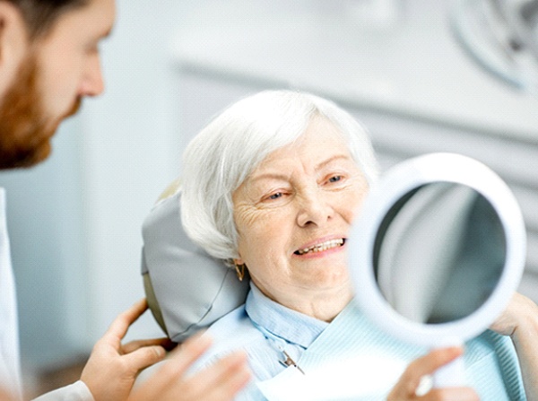 Senior woman examining new implant dentures in handheld mirror