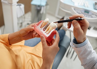 A patient holding tooth model while a dentist explains dental implant recovery
