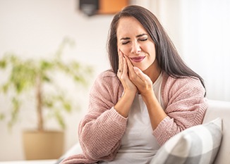 A woman cupping her cheek as she experiences oral pain