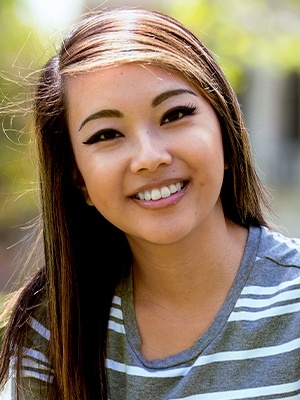 Young woman with gray striped shirt smiling outside