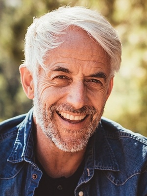 Older man outdoors laughing in denim shirt
