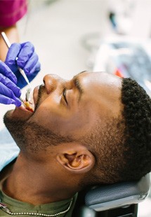 Woman in pink scrubs and blue gloves examining patient’s teeth