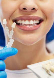 Nose-to-neck view of shade guide held to woman’s smile for veneers