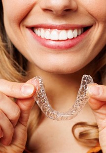 Nose-to-chest view of dentist holding model implant and touching her cheek
