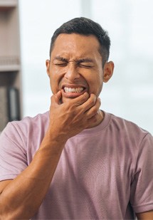 Man squinting and touching fingers to mouth in pain