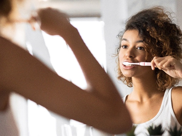 A young woman standing in front of her mirror brushing her teeth