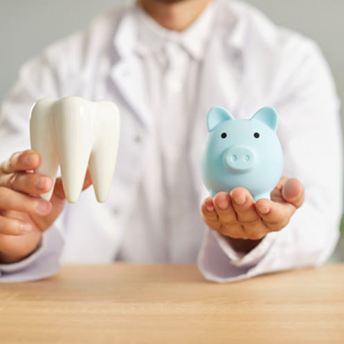 Dentist holding model tooth in one hand and piggy bank in the other