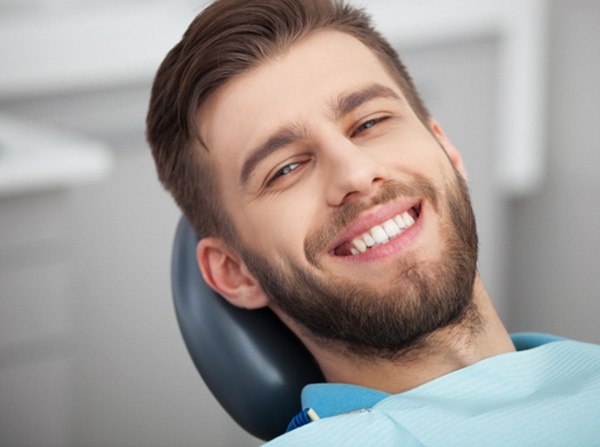 Bearded man leaning back in dental chair and smiling