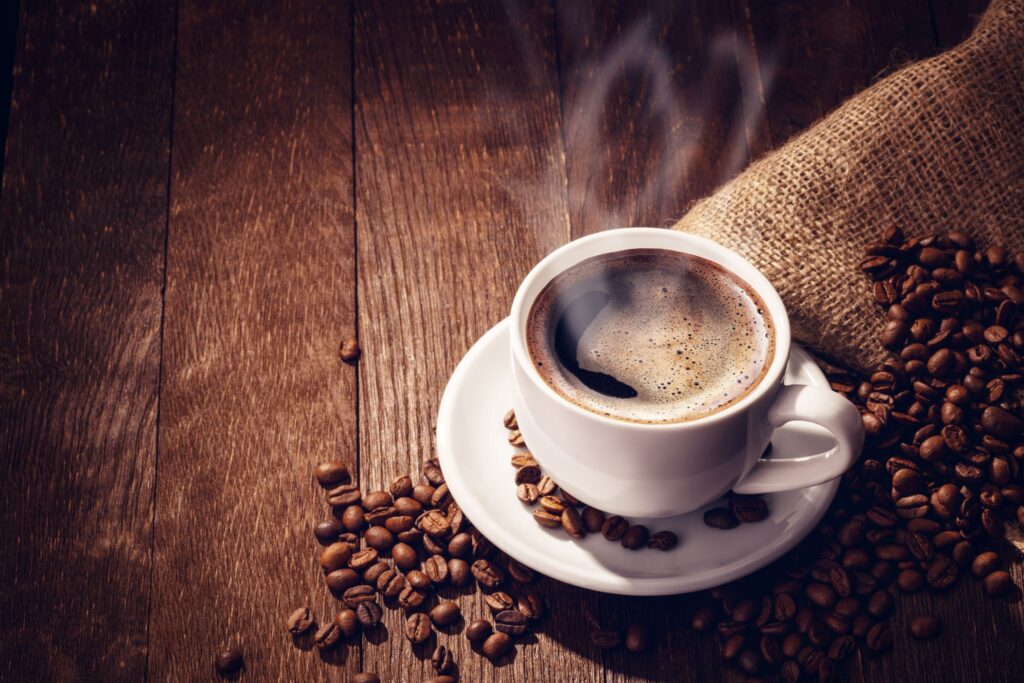 Cup of coffee on saucer next to coffee beans on wooden surface