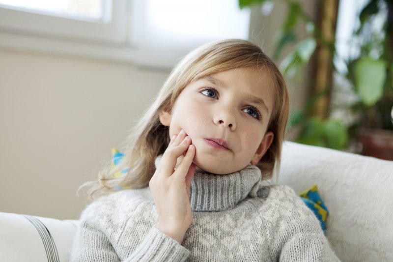 Little girl in sweater thoughtfully rubbing her aching jaw