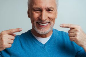 Man smiling and pointing to his white dentures