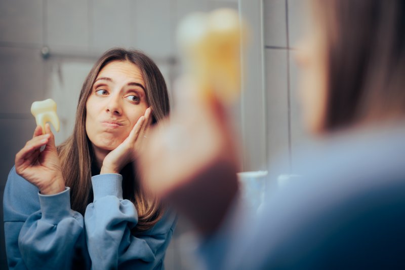 woman holding her cheek and tooth in her hand