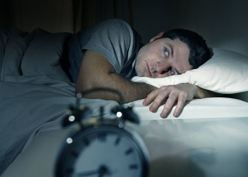 Man lying awake in bed looking at alarm clock