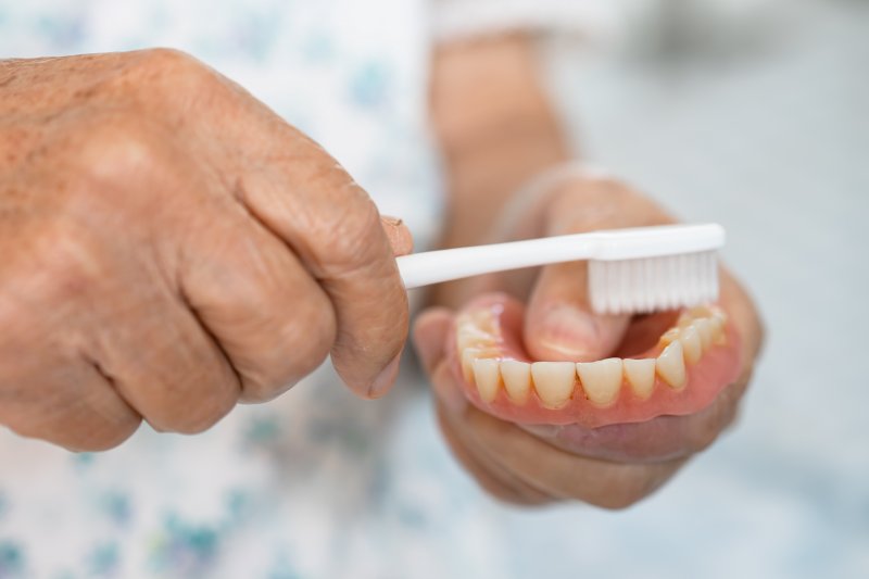 A closeup of hands brushing a denture with a toothbrush