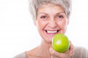 Woman with dental implants in Leesburg holding an apple.