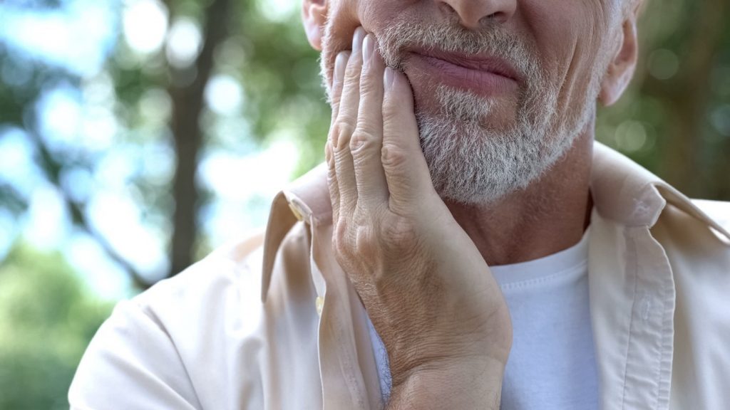person with jaw pain holding face